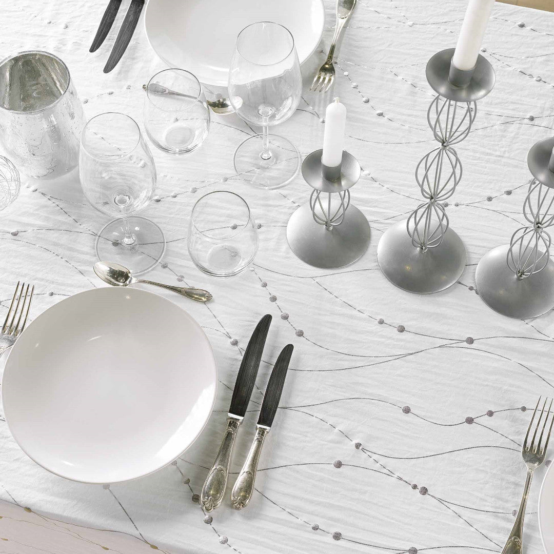 Nærbilde av borddekking med Firmament Metallic hvit duk med bølgende sølvtrykk